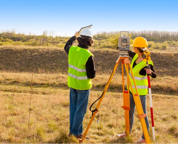 Surveyors in a field, performing commercial surveys in Bettendorf IA for a new development project